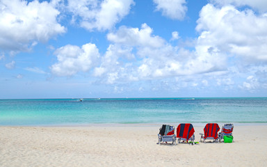 Fototapeta na wymiar Beach Chairs on White sand beach. Blue sea water and dramatic clouds. Oranjestad, Aruba. Famous Eagle Beach