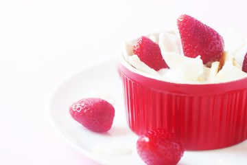 Healthy raw vegan dessert - banana and strawberry with coconut cream and coconut chips on pink background