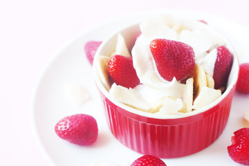 Healthy raw vegan dessert - banana and strawberry with coconut cream and coconut chips on pink background