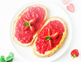 Slices of french bread with strawberry jam and mint on white background - healthy summer breakfest