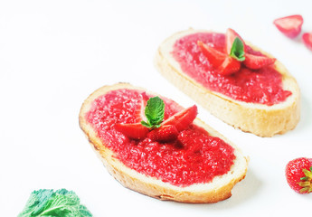 Slices of french bread with strawberry jam and mint on white background - healthy summer breakfest