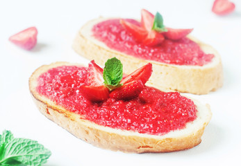 Slices of french bread with strawberry jam and mint on white background - healthy summer breakfest