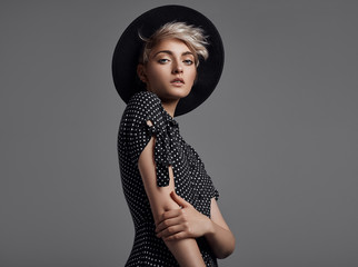 Fashion portrait of female model with blond short hair wear black hat and fashionable dress