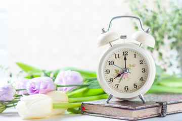 Retro alarm clock, notebook and spring flowers.