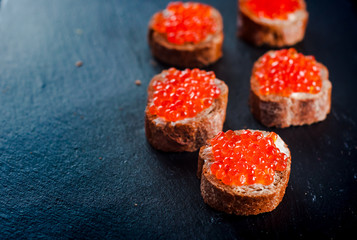 Red caviar on bread on slate background.