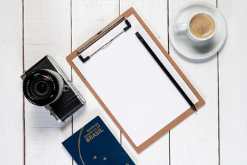 Camera on white wooden background. Note pad and pencil for travel planning. Brazilian passport.