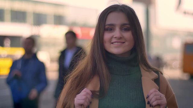 Awesome caucasian female is standing a side road and looking straight with happy face at camera, relaxing in city area, casual style