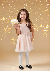 girl child is in christmas lights, yellow background, pink dress