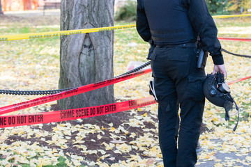 Police officer in the helmet standing by the crime scene closed by yellow and red cop tape.