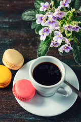 Obraz na płótnie Canvas Beautiful breakfast. Morning cup of coffee with colorful macarons, on with flowers on dark background with copy space.