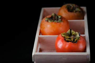 Persimmon ripe in a wooden box on a black background