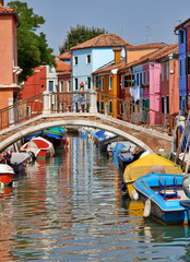 Fototapeta na wymiar Burano, Venice / Italy - August 2008: Ancient bridge over a canal and colorful facades