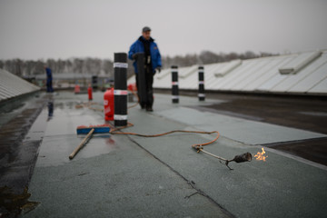 Flachdach Reparatur: Dachdecker verschweißt Dachabdichtung. Dachsanierung mit Gasbrenner.
