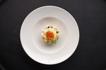 Traditional Russian salad Olivier with red caviar on top on black background