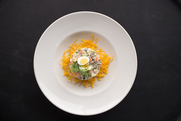 Traditional Russian salad Olivier with boiled egg on top on black background