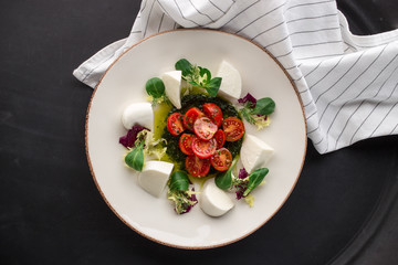 Italian caprese salad with sliced tomatoes, mozzarella cheese, basil, olive oil on black background