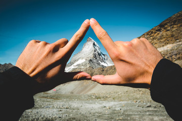 human hand forming a triangle in front of matterhorn mountain