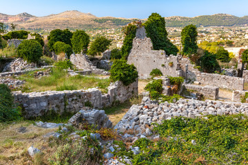 Fototapeta na wymiar The inner courtyard of the ancient city with dilapidated walls, the land overgrown with green grass with trodden paths, view from above. Summer landscape in Fortress Old Bar Town, Montenegro.