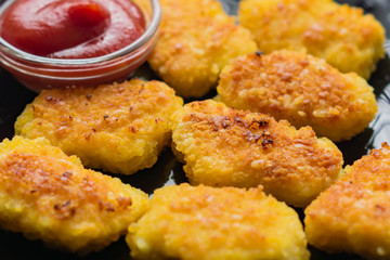 Fried crispy chicken nuggets with ketchup on black plate. Unhealthy food.