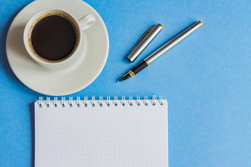 top view of cup of black coffee with notebook and pen on blue background. business concept with copy space