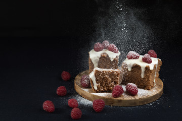 The home-made simple cake with the glazed surface decorated with fresh berries of raspberry. Cake is cut on portion pieces and laid out on a wooden support. A black background, it is isolated