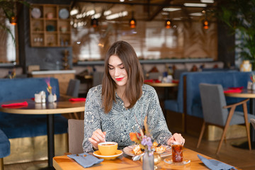 Young woman drinking coffee. Female holding cup. Sitting in coffee shop at wooden table. On table plate with breakfast. pleasant morning, the beginning of the working day