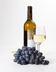 A glass of white wine, a bunch of grapes, an open bottle.