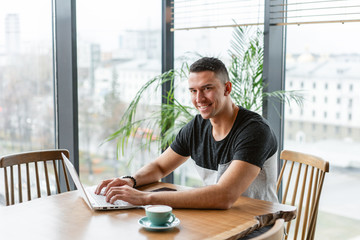 Young man drinking coffee from a Cup. Freelancer work on netbook in modern coworking. Programmer at remote job. Successful people, businessman in comfortable cafe. High large Windows
