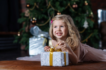 Little smiling girl with Christmas gift box lying on the floor on Christmas tree background