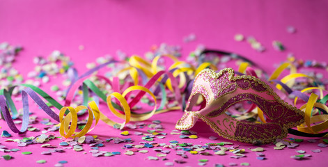 Carnival mask, streamers and confetti on pink background