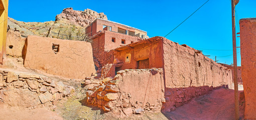The shabby walls of medieval mud houses of Abyaneh village with the ruins of ancient fort on the...