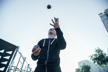 Calm sportsman throwing balls into the air and catching them