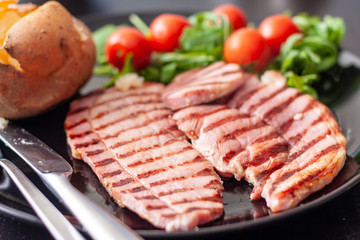 Close-up of a grilled gammon steak with a baked potato and salad