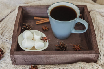 Cup of coffee on rustic wooden tray, sweet marshmallow and warm woolen sweater. Cozy autumn or winter weekend or holidays at home. Fall home decoration with hot drink mug. Hygge morning style concept