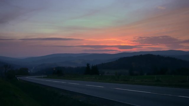Car on the road between hills. Beautiful sunset with colorful sky.