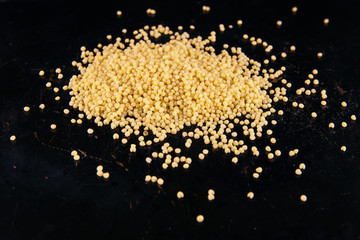 A handful of yellow millet groats on a black iron background.