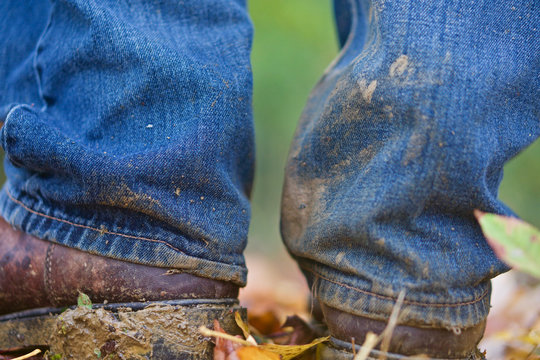 Closeup of legs of a man with dirty boots and dirty blue denim jeans standing on the forest.