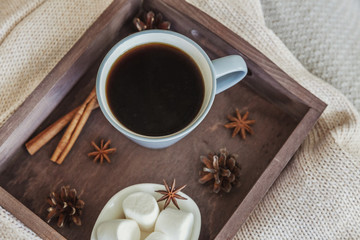 Cup of coffee on rustic wooden tray, sweet marshmallow and warm woolen sweater. Cozy autumn or winter weekend or holidays at home. Fall home decoration with hot drink mug. Hygge morning style concept