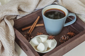 Cup of coffee on rustic wooden tray, sweet marshmallow and warm woolen sweater. Cozy autumn or winter weekend or holidays at home. Fall home decoration with hot drink mug. Hygge morning style concept