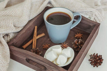 Fototapeta na wymiar Cup of coffee on rustic wooden tray, sweet marshmallow and warm woolen sweater. Cozy autumn or winter weekend or holidays at home. Fall home decoration with hot drink mug. Hygge morning style concept