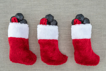 Three red and white plush Christmas stockings, with coal shaped candy spilling out, on light linen...
