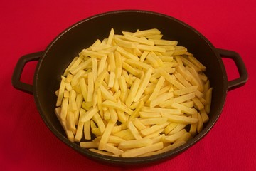 Precooked frozen yellow sliced potatoes in a big black pan with handles isolated on red surface