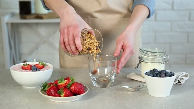 Woman preparing tasty breakfast with granola, yogurt and blueberries at table
