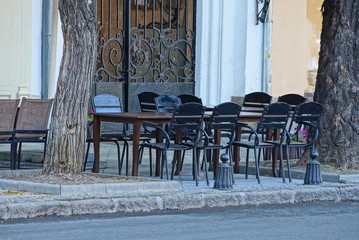 black chairs and tables are on the sidewalk by an asphalt road