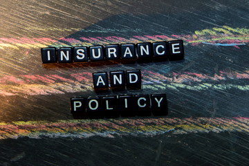 Insurance and Policy on wooden blocks. Cross processed image with blackboard background. Inspiration, education and motivation concepts