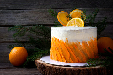 Christmas cake with  oranges and fir branches on a wooden background.