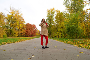 Fototapeta premium Young girl in coat standing on a long road in autumn Park.
