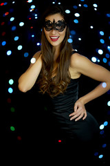 beautiful young smiling woman in a sexy face mask on a black background in New Year's Eve