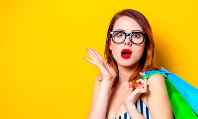 redhead woman in black glasses with colour shopping bags on yellow background