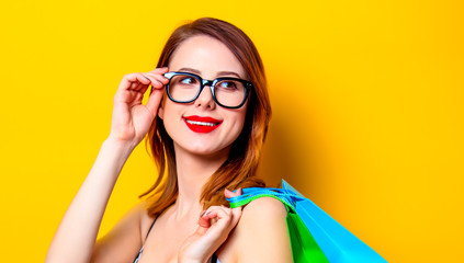 Redhead woman in black glasses with colour shopping bags on yellow background